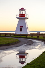 Vertical view of a small red and white lighthouse reflected in puddle seen at sunset, Carleton-sur-Mer, Quebec, Canada