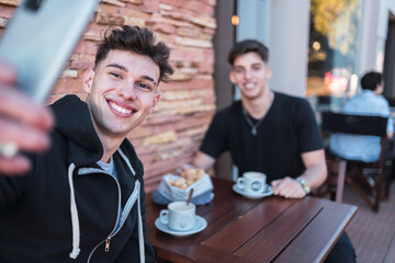 Two young men smiling as they take a selfie at an outdoor bar.