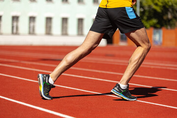 Obraz premium Cropped image of male athlete, runner training at public stadium, sport court or running track outdoors. Summer sport games. Man's legs
