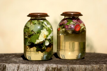 Two glass jars with sun tea. Solar tea is water heated by solar energy, which contains various tree leaves, flowers, medicinal herbs, fruits. 
