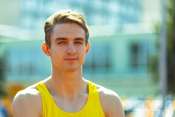 Close-up young Caucasian man, male athlete, runner at public stadium, sport court or running track outdoors. Summer sport games.