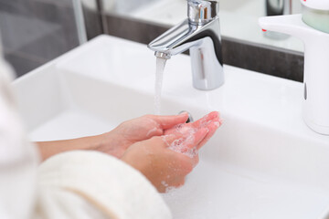 Woman washing her hands under water from tap in bathroom closeup