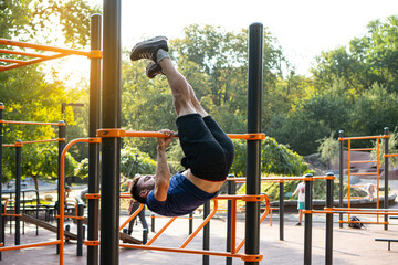 Fit man doing lifting with a flip on a horizontal bar at the open air gym.