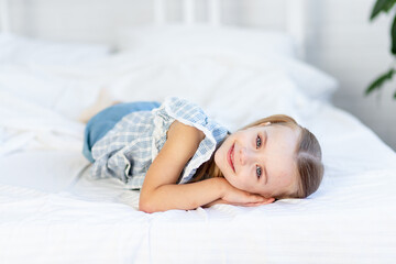 a girl child is lying on the bed at home on a white cotton bed or has woken up in the morning and is smiling sweetly