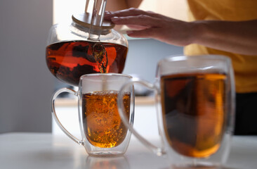Woman pouring black tea from teapot into cup closeup