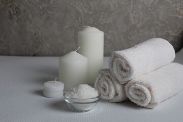 Obraz na płótnie Canvas Spa treatments care home body llax massage. White candle towels in a roll of salt and scrub on a gray background with space for copyspace text. Beauty parlour