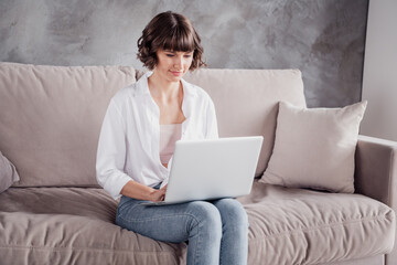 Naklejka premium Photo portrait woman wearing white shirt jeans sitting on sofa at home smiling using laptop