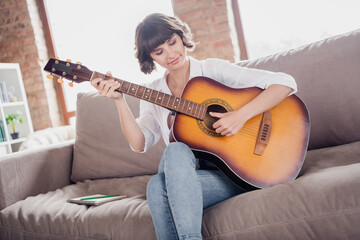 Photo portrait young woman playing acoustic guitar sitting on sofa alone at home spending free time