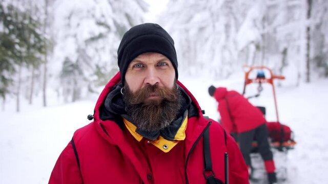 Man paramedic from mountain rescue service outdoors in winter in forest, looking at camera.