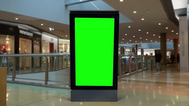 Green Screen Panel Inside Shopping Mall With People Walking. People walking behind a digital panel green screen inside a shopping mall.