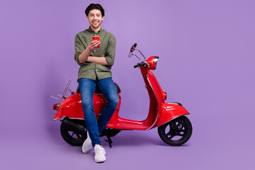 Fototapeta na wymiar Full length photo of positive cheerful young man cool hold hand smartphone enjoy isolated on purple color background