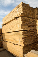 Stacks of timber and edged boards of coniferous wood are yellow against the blue sky. Construction production of textures.