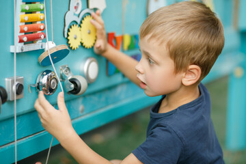 The child enthusiastically studies the Busy Board, a children's development board, develops motor...