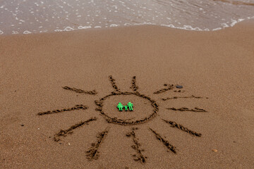 symbol of the sun and a family by the sea. Painted sun on the sand, sea coast, figure of a green family, sea waves