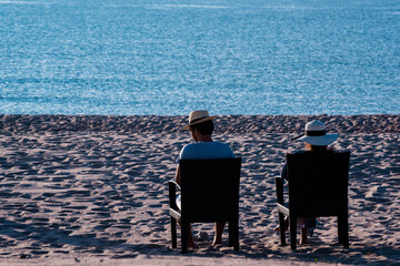 Couple Sitting On Chairs At Beach Against Sky