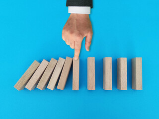 Businessman stopping falling dominos in a conceptual image, chain reaction in business concept