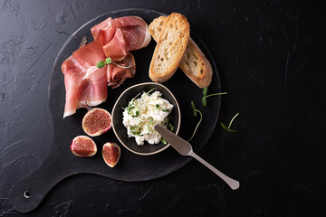 Dry cured ham with slices of bread on a black background, Italian appetizer prosciutto with fruit and cheese. - obrazy, fototapety, plakaty