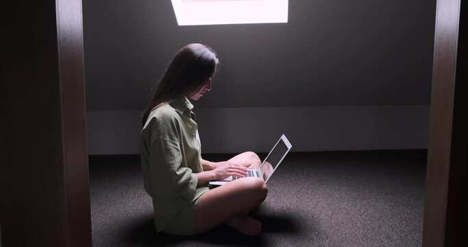 Woman using laptop sitting cross legged on floor with skylight window letting the sun shine in