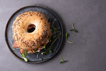 Delicious snack concept, bagel with cream cheese, dry cured ham and microgreens on a plate on a...
