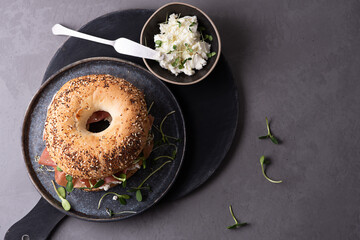 Plate with bagel with cream cheese, dry cured ham and microgreens on a gray background, delicious snack concept.