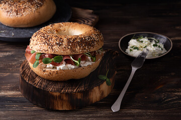 Sandwich with ricotta, prosciutto and microgreens, ham bagel for breakfast on a dark wooden...