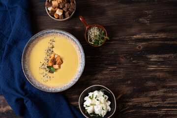 Plate of squash cream soup with croutons, cheese and microgreens on a dark wooden background, healthy vegetarian puree soup.