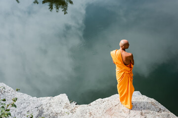 high angle view of buddhist monk meditating on rocky cliff over water