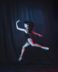 Young and graceful female ballet dancer in motion isolated on dark background in neon light. Art,...