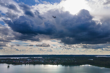 The plane flies over the lake and the city, high in the clouds from which the sun shines. the concept of air transportation and the safety of movement by air.