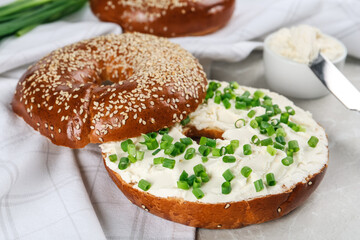 Delicious bagel with cream cheese and green onion on light table, closeup