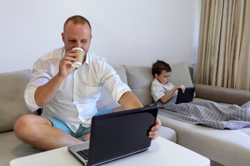Photo of a busy young man with son at home. Shot of a boy playing while his father is working on a computer. Young dad with toddler child working on the computer from home.