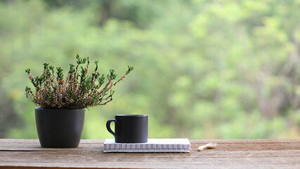 black coffee mug with heathers plant in black pot on wooden table at outdoor