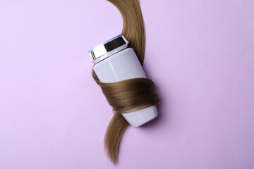 Bottle wrapped in lock of hair on violet background, top view. Natural cosmetic product