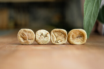 four round shriveled dried dried figs stand in a horizontal row on a wooden table in a kitchen with a houseplant