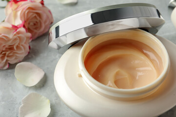 Jar of hair care cosmetic product and flowers on grey table, closeup
