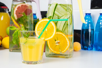 on a white table, a glass of freshly squeezed orange juice with a straw and jugs of refreshing lemonade