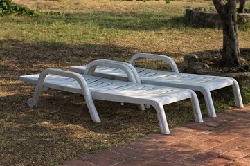 A pair of white plastic sun loungers under the shade of trees in the garden (Umbria, Italy, Europe) - 458536414