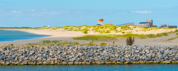 Sand dunes with grass and yellow white sand along the coast of an island below a blue sky in bright sunlight in summer, Marker Wadden, Lelystad, Flevoland, Netherlands, september 20, 2021 © Naj