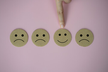 Closeup hand select happy face smile face icon paper cut on pink background, Customer service evaluation and satisfaction survey concept.