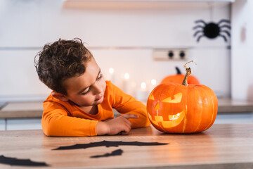 Portrait of a little boy dressed in a pumpkin t-shirt looking at his pumpkin decorated and lit up for the halloween party at home. 