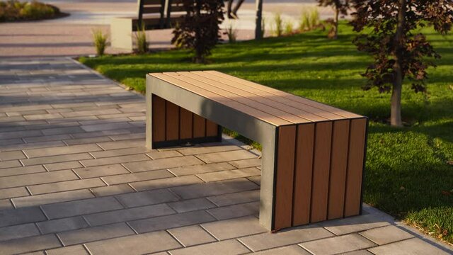 Modern wooden benches on the lawn in the park. Stylish new bench in city recreation area on sunrise or sunset. Urbanism theme public space landscape design. No people on empty street sidewalk.