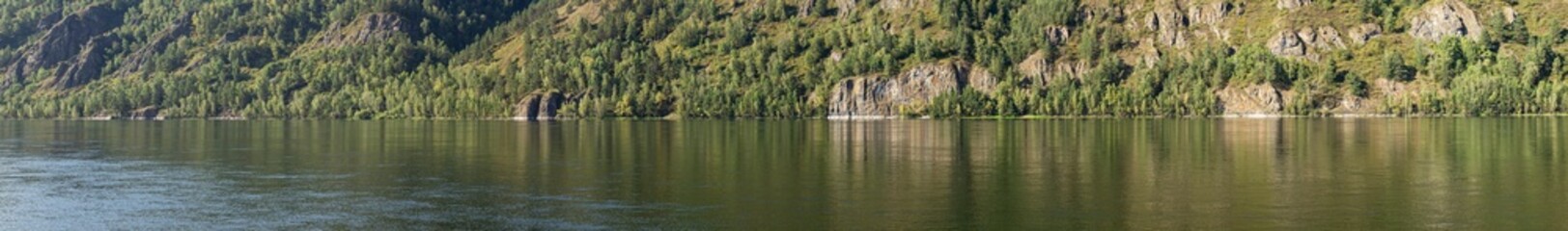 A wide panorama of the rocky bank of a large river.