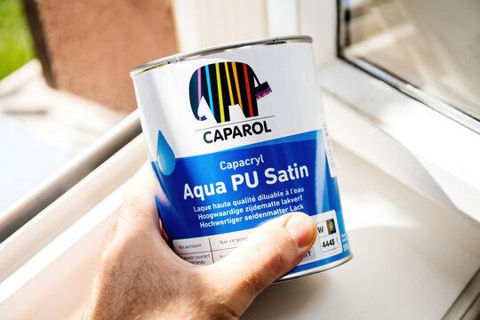 Paris, France - Sep 8, 2021: POV male hand hear window of new unopened metal can with Caparol Aqua PU satin for home redecoration and re-paining - defocused blur background