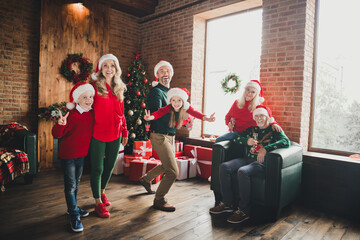 Photo of friends childhood grandparents retired pensioner little grandchildren husband wife v-sign wear santa claus hat noel house indoors