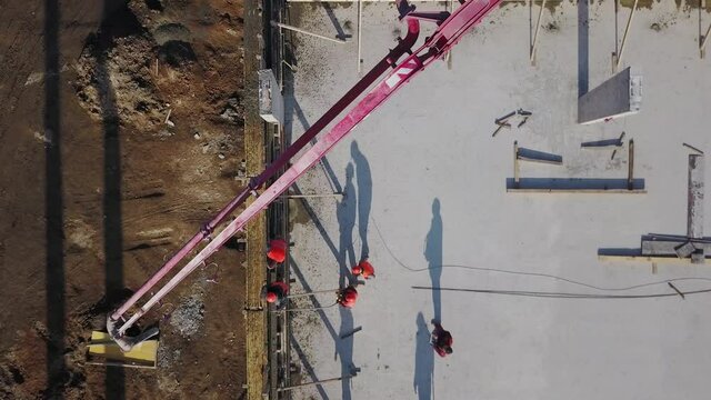 Aerial of concrete boom pump crane arm truck with outriggers pouring building mixture into a formwork. Construction workers pour reinforced concrete walls of tribune stage. View from above.