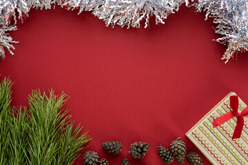 Christmas composition. A box with a gift and spruce branches on a red background. Spruce cones and Christmas decorations. Flat lay, top view, space for text
