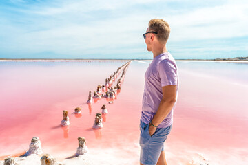 A young man walks on a salty pink lake with a blue sky. A peaceful landscape and relaxation