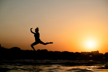 Happy girl having fun and jumps at sunset beach in sunlight. Summer vacation and healthy lifestyle concept. Empty space for text