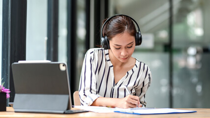 Front view of young Asian businesswoman wearing headphones listen to music while working holding a...