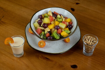 delicious dessert, refreshing fruit salad, natural colors, different textures and cuts, served in a crockery container, white plate decorated with small oranges, crispy natural cereals, yogurt served 